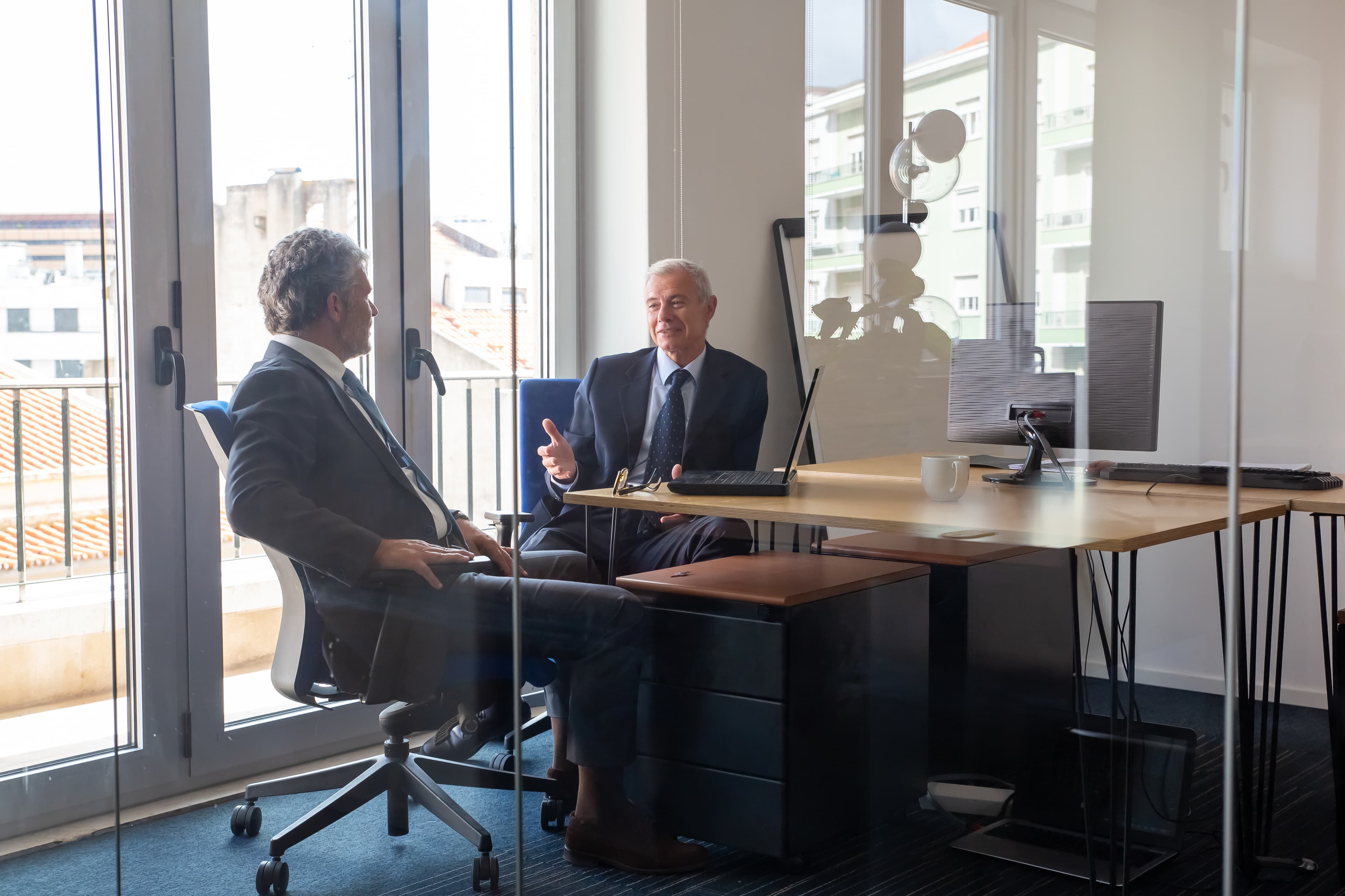 friendly-mature-business-partners-meeting-office-sitting-workplace-with-laptop-talking-view-through-glass-wall-business-portrait-concept.jpg